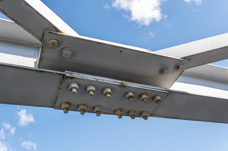A bolted splice plate joining white steel members, against a blue sky.