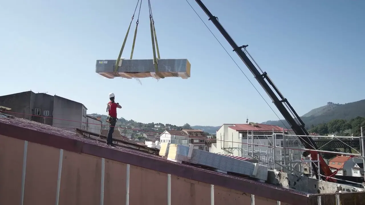 A crane lowering a load onto a roof under construction.