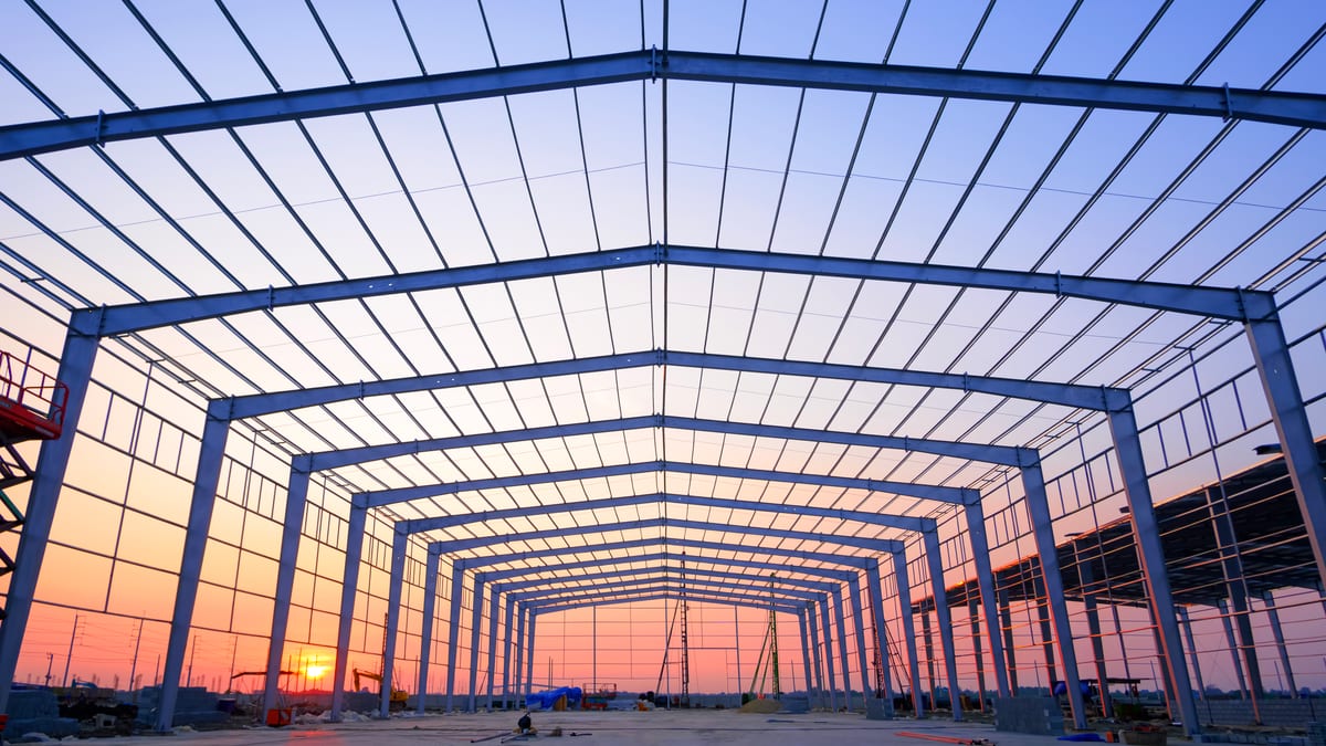 A run of steel portal frames, erected and braced, seen along their length at sunset.