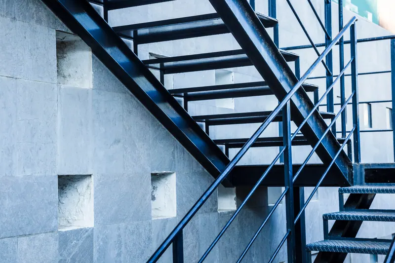 A steel stair with open treads and a steel balustrade beside a stone-clad wall.
